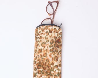May include: A glasses case with a leopard print pattern in shades of brown and tan, with a black zipper and a pair of eyeglasses. The eyeglasses have a brown frame.