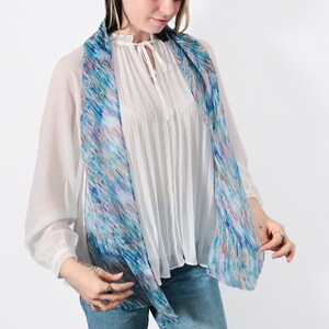 May include: A white blouse with a blue and white patterned scarf. The scarf is tied around the neck and hangs down the front of the blouse.