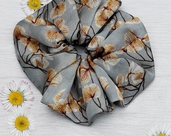 May include: A gray hair scrunchie with a floral pattern featuring white and brown flowers.
