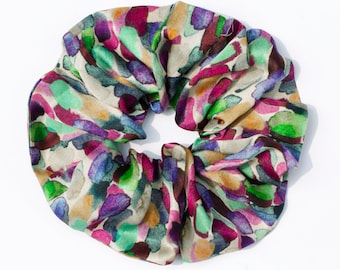 May include: A colorful hair scrunchie with a watercolor-like pattern in shades of green, purple, pink, and brown. The scrunchie is made of a soft, silky fabric.