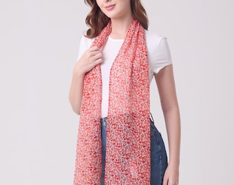 May include: A sheer red scarf with a floral pattern. The scarf is draped around the neck and shoulders. The scarf is made of a lightweight material and is a vibrant accessory.