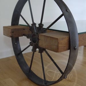 Pode incluir: Uma mesa de centro r&uacute;stica feita de uma roda de carro&ccedil;a reutilizada, t&aacute;buas de madeira e um tampo de vidro. A roda &eacute; pintada de preto e tem um acabamento desgastado. As t&aacute;buas de madeira s&atilde;o tingidas de uma cor marrom natural. O tampo de vidro &eacute; transparente e adiciona um toque moderno &agrave; mesa.