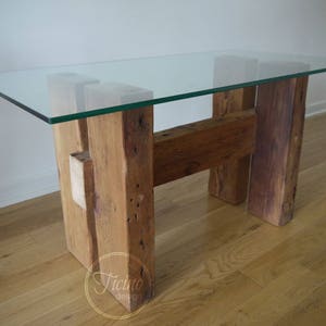 May include: A glass-topped table with a rustic wooden base. The table is rectangular and made from reclaimed wood.