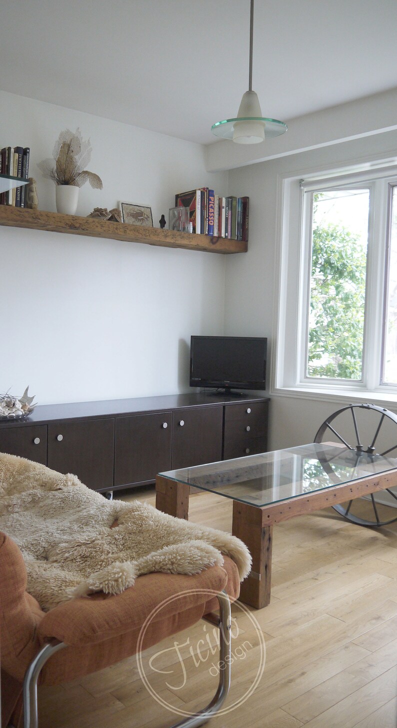Pode incluir: Uma sala de estar com uma prateleira de madeira marrom, um arm&aacute;rio marrom escuro com gavetas, uma televis&atilde;o de tela plana, uma mesa de centro com tampo de vidro e base de madeira, uma cadeira de couro marrom com uma manta de pele de carneiro e uma janela com vista para as &aacute;rvores.