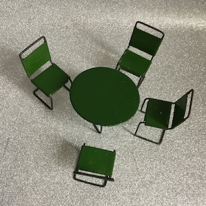 Peut inclure: Un ensemble de patio miniature en métal vert, comprenant une table ronde et quatre chaises. Les chaises ont un design simple avec un siège et un dossier. La table et les chaises sont peintes en vert uni.