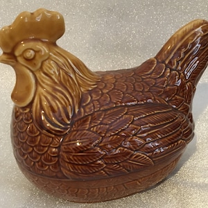 May include: A brown ceramic chicken shaped dish with detailed feathering. The chicken has a light brown comb and wattle.