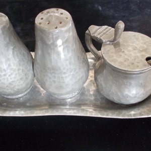 Peut inclure: Un ensemble de salière et poivrière en métal martelé argenté avec un pot à crème et une cuillère assortis sur un plateau.