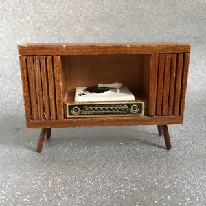 Puede incluir: Una consola de tocadiscos de madera en miniatura con un plato blanco y un disco negro. La consola tiene un acabado de madera marrón y cuatro patas.