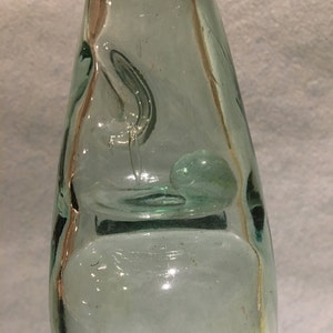 Puede incluir: Una botella de vidrio transparente con una superficie texturizada. La botella tiene una forma única con un fondo redondeado y un cuello estrecho.