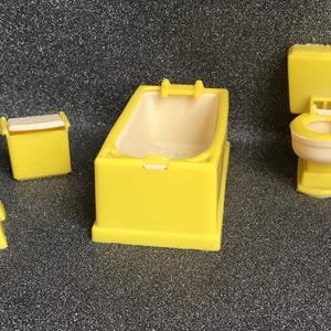 May include: A set of yellow miniature bathroom furniture, including a bathtub, toilet, and a small cabinet. The bathtub has a light beige interior. The toilet has a light beige toilet bowl. The set is made of plastic.