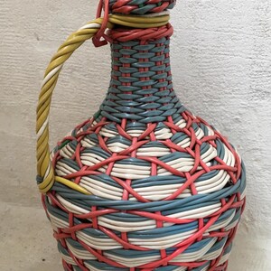 Könnte beinhalten: Eine dekorative gewebte Flasche mit Henkel und Verschluss. Die Flasche besteht aus gewebtem Kunststoff in Blau, Weiß, Rot und Gelb. Der Griff ist gelb und weiß, und der Verschluss ist rot und blau.