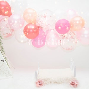 Pode incluir: Um tipi branco com acabamento em renda fica sobre uma superfície branca com uma estrutura de cama branca e um cobertor branco felpudo. Balões rosa, pêssego e transparentes com confete são enfiados na parte superior da imagem. O texto "BY TONYA MARIE" é visível no centro da imagem.