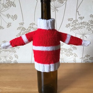 May include: A red and white striped knitted bottle cozy with a white turtleneck. The cozy is on a wine bottle.