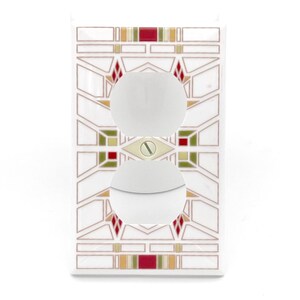May include: White electrical outlet cover with a geometric design in red, green, and gold. The cover has two circular openings for the outlets and a screw in the center. The design is reminiscent of stained glass.
