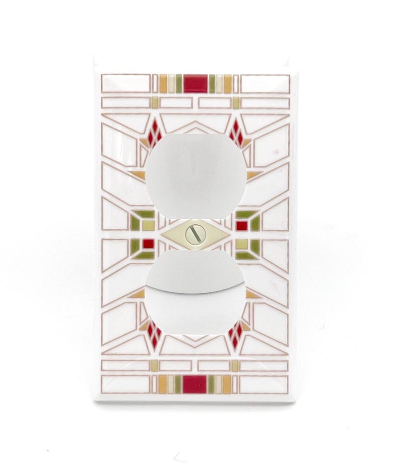 May include: White electrical outlet cover with a geometric design in red, green, and gold. The cover has two circular openings for the outlets and a screw in the center. The design is reminiscent of stained glass.