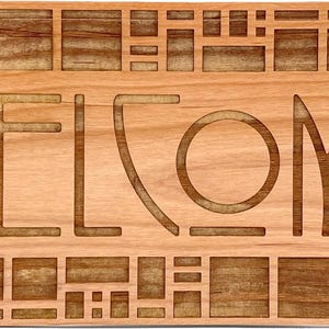 Puede incluir: Un letrero de bienvenida rectangular de madera con la palabra "WELCOME" tallada en la madera. El letrero tiene un color marr&oacute;n claro con un dise&ntilde;o geom&eacute;trico en la parte superior e inferior.