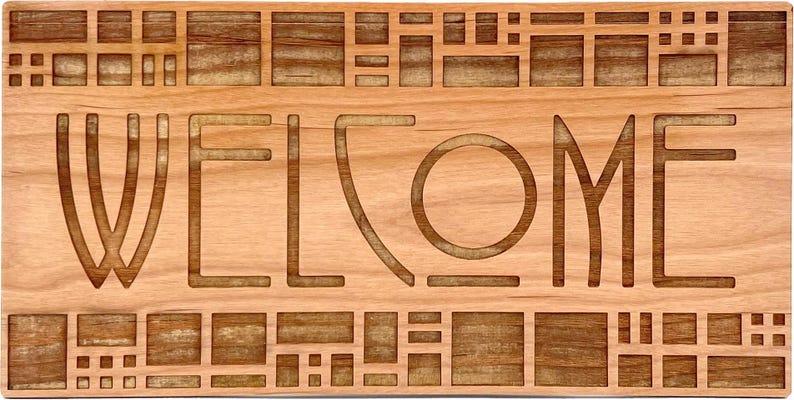 Puede incluir: Un letrero de bienvenida rectangular de madera con la palabra "WELCOME" tallada en la madera. El letrero tiene un color marr&oacute;n claro con un dise&ntilde;o geom&eacute;trico en la parte superior e inferior.