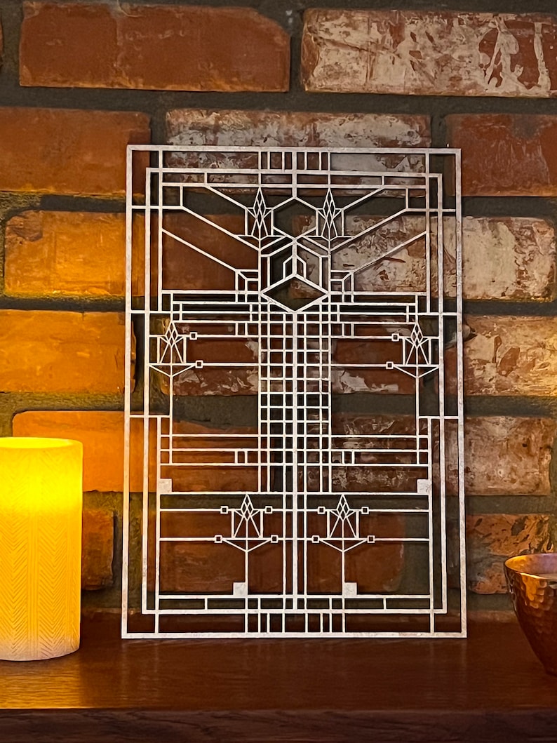 Pode incluir: Uma pe&ccedil;a de arte de parede de metal prateado com um design geom&eacute;trico. O design lembra uma janela ou uma tela, com um padr&atilde;o repetitivo de quadrados e ret&acirc;ngulos. A pe&ccedil;a de arte est&aacute; montada em uma parede de tijolo.