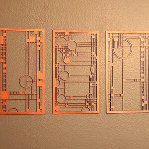 May include: Three geometric wall art pieces in a light orange color. Each piece features a different design with a repeating pattern of squares and circles.
