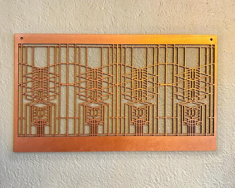Puede incluir: Una pieza de arte mural rectangular de color cobre con un dise&ntilde;o geom&eacute;trico. La obra de arte presenta un patr&oacute;n repetitivo de formas rectangulares y angulares, creando un efecto de capas. Se ven dos peque&ntilde;os agujeros en la parte superior para colgar. La pieza est&aacute; montada en una pared clara.
