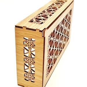 May include: A rectangular wooden box featuring intricate laser-cut geometric star patterns on the top and side panels. The light-colored wood grain is visible throughout the structure, which is assembled with visible interlocking joints.