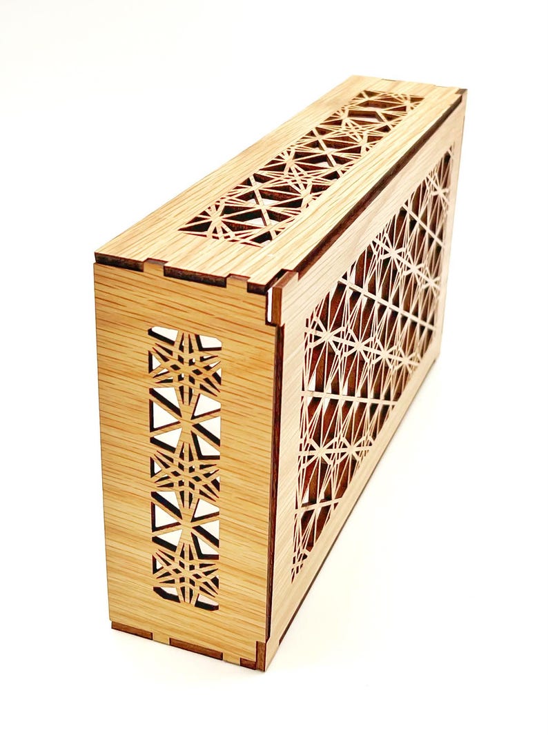 May include: A rectangular wooden box featuring intricate laser-cut geometric star patterns on the top and side panels. The light-colored wood grain is visible throughout the structure, which is assembled with visible interlocking joints.