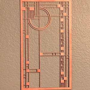 Puede incluir: Una decoraci&oacute;n de pared de madera con un dise&ntilde;o geom&eacute;trico en color marr&oacute;n rojizo. El dise&ntilde;o presenta un c&iacute;rculo con un c&iacute;rculo m&aacute;s peque&ntilde;o en su interior, y una serie de cuadrados y rect&aacute;ngulos.
