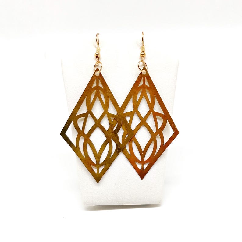 May include: A pair of gold-toned earrings with a geometric diamond shape and intricate cut-out designs.