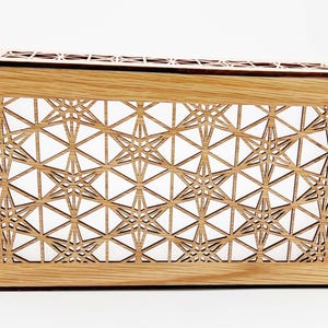 May include: A rectangular wooden box featuring a light brown natural wood grain finish and an intricate laser-cut geometric lattice pattern on the front panel. The design consists of repeating star-like shapes formed by thin intersecting lines.