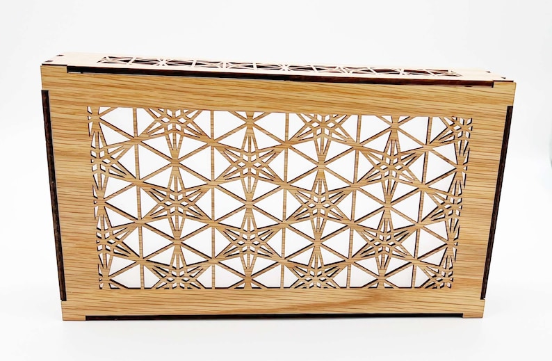 May include: A rectangular wooden box featuring a light brown natural wood grain finish and an intricate laser-cut geometric lattice pattern on the front panel. The design consists of repeating star-like shapes formed by thin intersecting lines.
