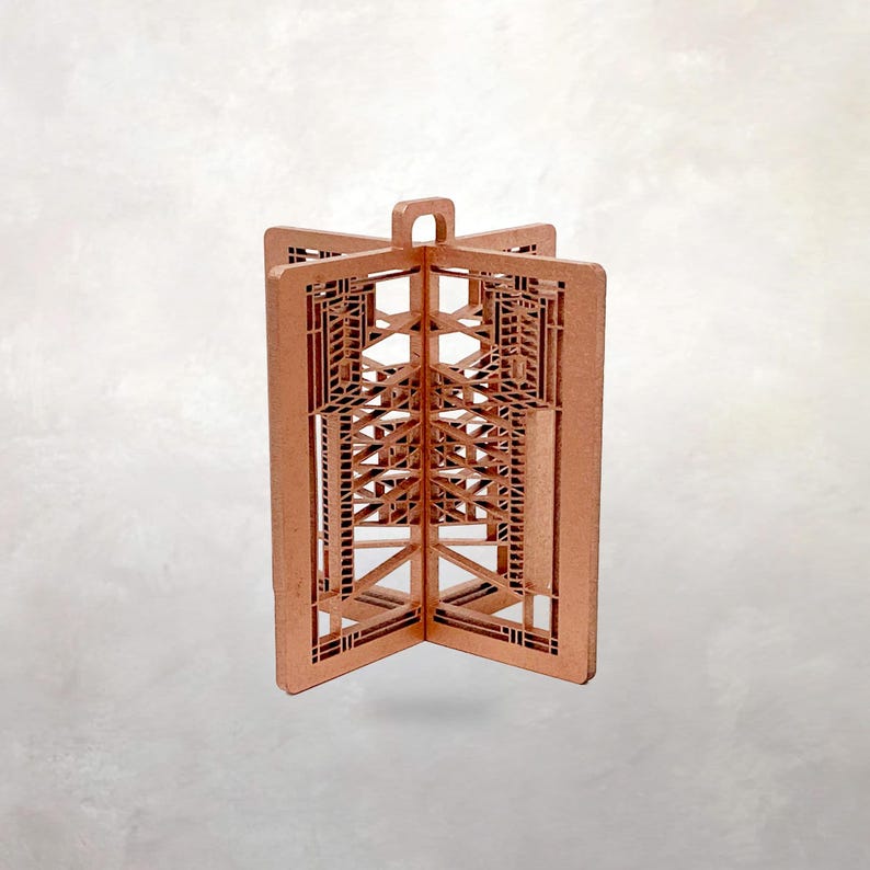 May include: A copper-colored, geometric ornament with an open, architectural design. The ornament is made of several connected panels, forming a three-dimensional shape with intricate cut-out patterns. It has a loop at the top for hanging.