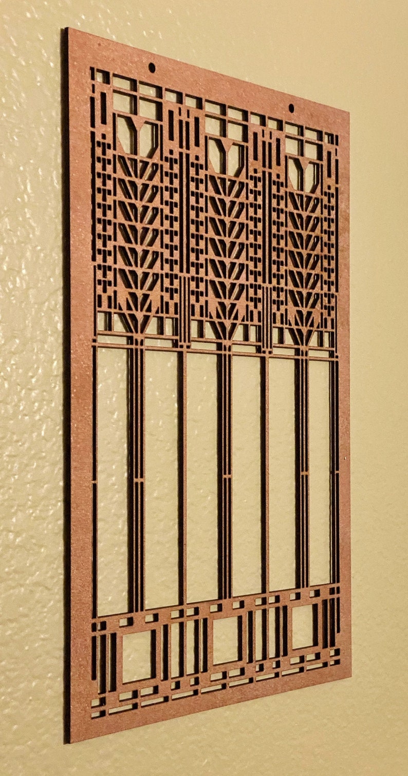 May include: A rectangular, laser-cut wooden panel with a geometric design. The panel features a repeating pattern of vertical lines and stylized leaf shapes, with a warm, reddish-brown color. The design is reminiscent of Art Deco or Craftsman style.