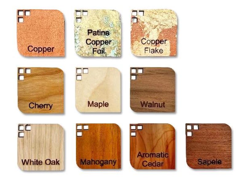 May include: A collection of eleven square material samples with rounded corners and small cutouts. The samples include copper, patina copper foil, copper flake, cherry, maple, walnut, white oak, mahogany, aromatic cedar, and sapele wood finishes.