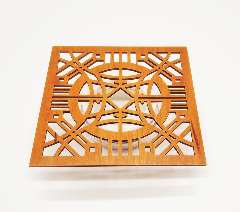 May include: A square wooden coaster with a geometric openwork design. The coaster is a warm, medium brown colour and features intersecting lines and circular shapes. The design is symmetrical and intricate, creating a decorative and functional item.