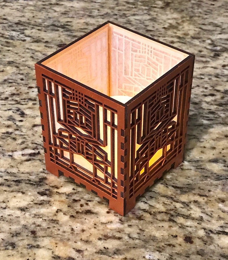 May include: A square, wooden candle holder with intricate geometric cutouts. The warm, amber glow of a light source inside illuminates the detailed design. The exterior is a rich, dark brown.