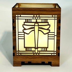 May include: A wooden box with a dragonfly design. The box is made of dark brown wood and features a dragonfly silhouette in the center, with a yellow light shining through the design. The box has a rectangular shape.