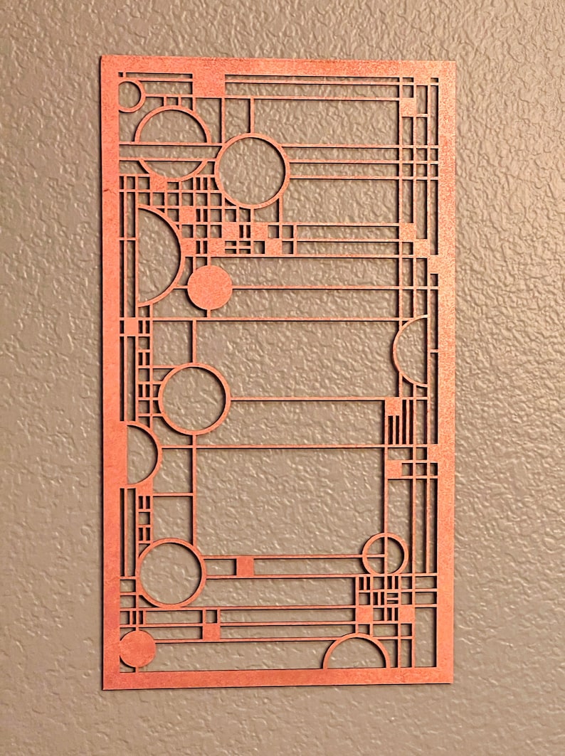 Puede incluir: Una pieza de arte mural rectangular de color cobre con un dise&ntilde;o geom&eacute;trico. La obra de arte presenta una serie de c&iacute;rculos, cuadrados y l&iacute;neas rectas, creando un patr&oacute;n abstracto. La pieza est&aacute; hecha de un material delgado y est&aacute; montada en una pared texturizada de tono neutro.