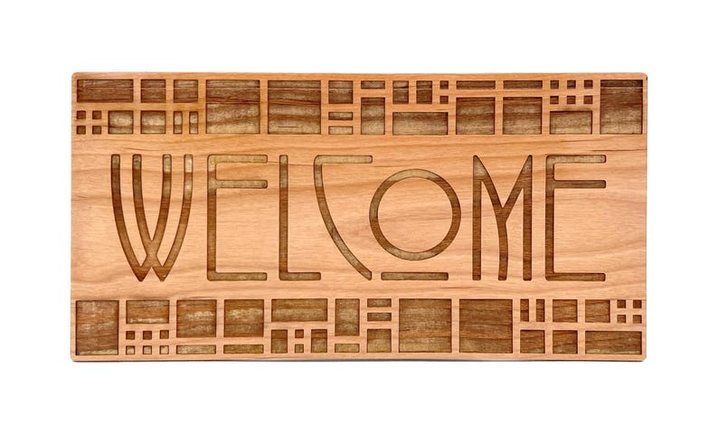 Puede incluir: Un letrero rectangular de madera con la palabra &laquo;WELCOME&raquo; tallada en la superficie. El letrero es de madera de color marr&oacute;n claro y presenta un patr&oacute;n geom&eacute;trico alrededor de los bordes y entre las letras.