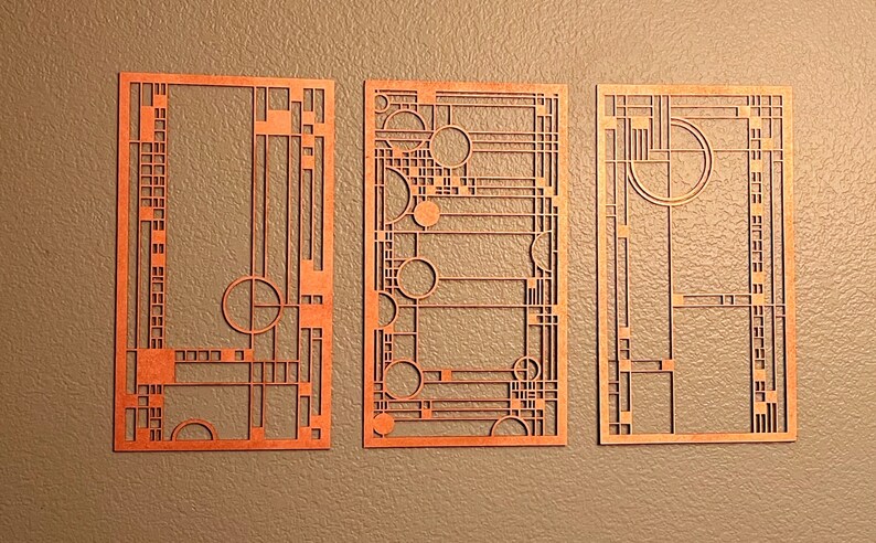 May include: Three copper-colored, geometric art deco panels. Each panel features a unique design of lines, rectangles, and circles. The panels are displayed against a neutral, textured background, showcasing the intricate cut-out patterns.
