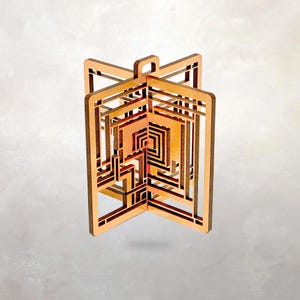 May include: A geometric wooden ornament with a layered design. The ornament features a series of interconnected rectangular shapes and a warm color palette of light brown, orange, and red. It has a loop at the top for hanging.