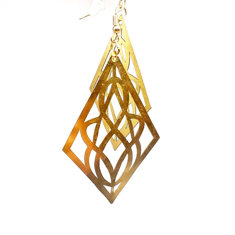 May include: Gold-toned earrings with a geometric diamond shape and intricate cut-out design.
