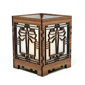 May include: A wooden lantern with a geometric design. The lantern is square with intricate cutouts and a light-coloured interior. The wood has a warm, brown tone, and the design is reminiscent of an art deco style.