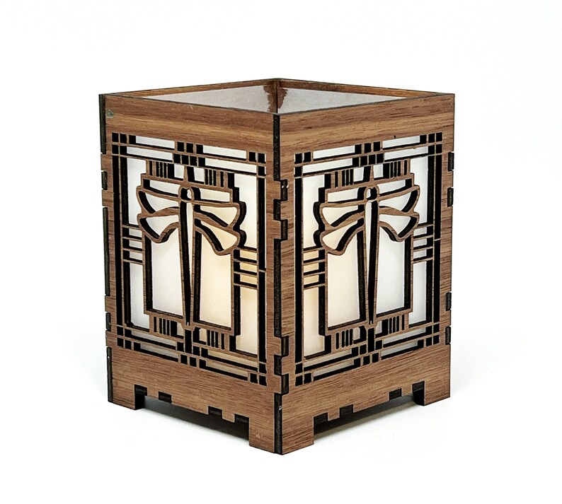 May include: A wooden lantern with a geometric design. The lantern is square with intricate cutouts and a light-coloured interior. The wood has a warm, brown tone, and the design is reminiscent of an art deco style.