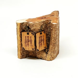 K&ouml;nnte beinhalten: Ein Paar Holzohrringe mit einem Waldmotiv. Die Ohrringe sind rechteckig und haben eine braune Holzoptik. Das Waldmotiv ist in das Holz ge&auml;tzt und zeigt eine Vielzahl von B&auml;umen. Die Ohrringe h&auml;ngen an einem Holzstamm.
