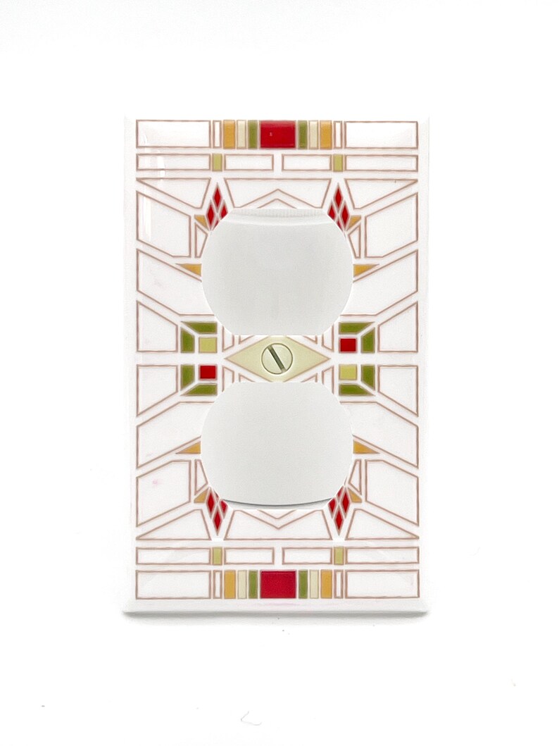 May include: A white electrical outlet cover with a geometric design in red, green, and gold. The cover features two white, oval-shaped outlets and a gold screw in the center. The design is reminiscent of stained glass.