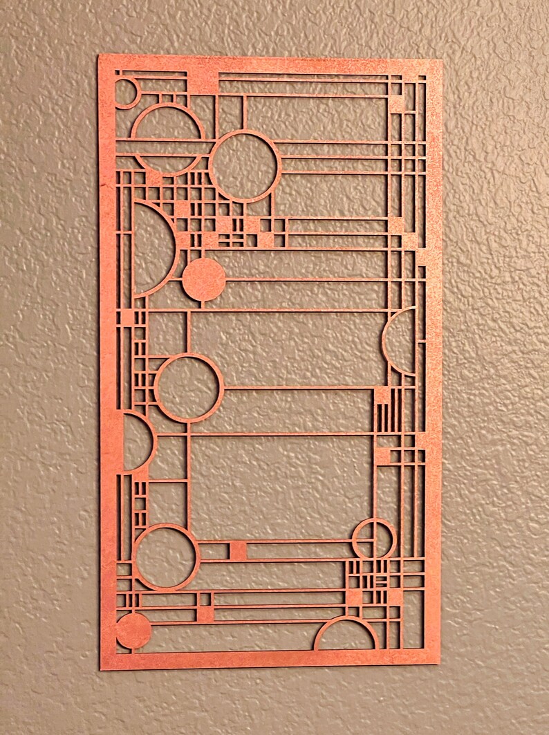 May include: A copper-colored, rectangular wall art piece with a geometric design. The art features a series of circles, squares, and straight lines, creating an abstract pattern. The piece is mounted on a neutral-colored wall.