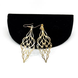May include: A pair of gold-tone dangle earrings with a delicate, intricate design. The earrings are made of metal and have a teardrop shape.