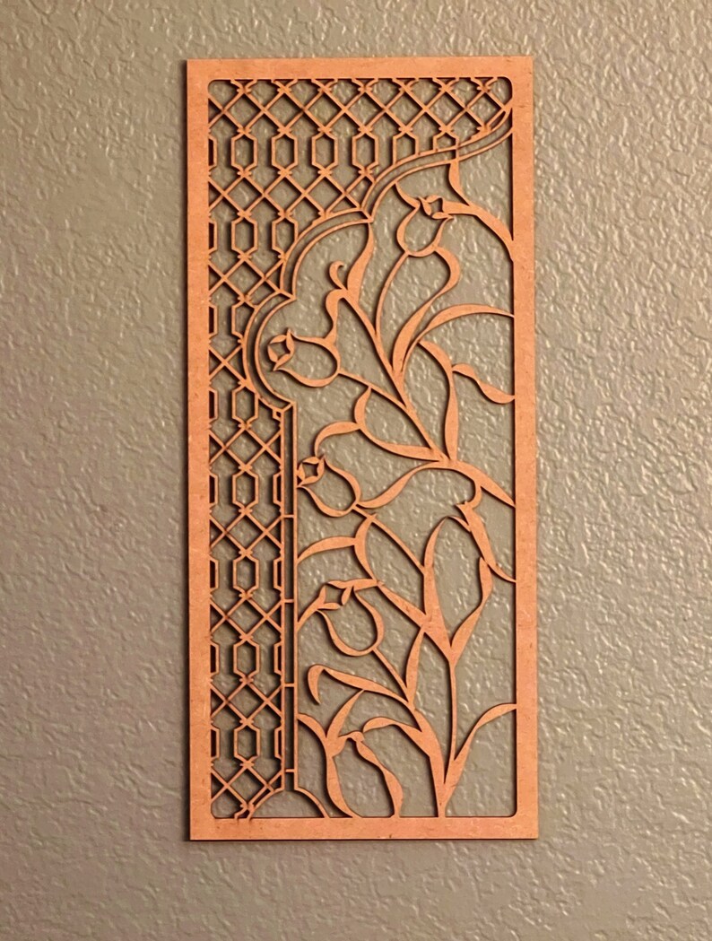 Pu&ograve; includere: Pannello rettangolare in legno tagliato al laser con un design intricato. Il pannello presenta un reticolo geometrico a sinistra e motivi floreali a destra. Il legno ha una calda tonalit&agrave; marrone-rossastra e il disegno &egrave; ritagliato.
