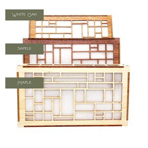 Peut inclure: Trois bo&icirc;tes en bois empil&eacute;es. La bo&icirc;te sup&eacute;rieure est en ch&ecirc;ne blanc, celle du milieu en sapelli et celle du bas en &eacute;rable. Chaque bo&icirc;te pr&eacute;sente un motif g&eacute;om&eacute;trique avec des d&eacute;coupes rectangulaires et carr&eacute;es. Le texte "WHITE OAK", "SAPELE" et "MAPLE" est visible.