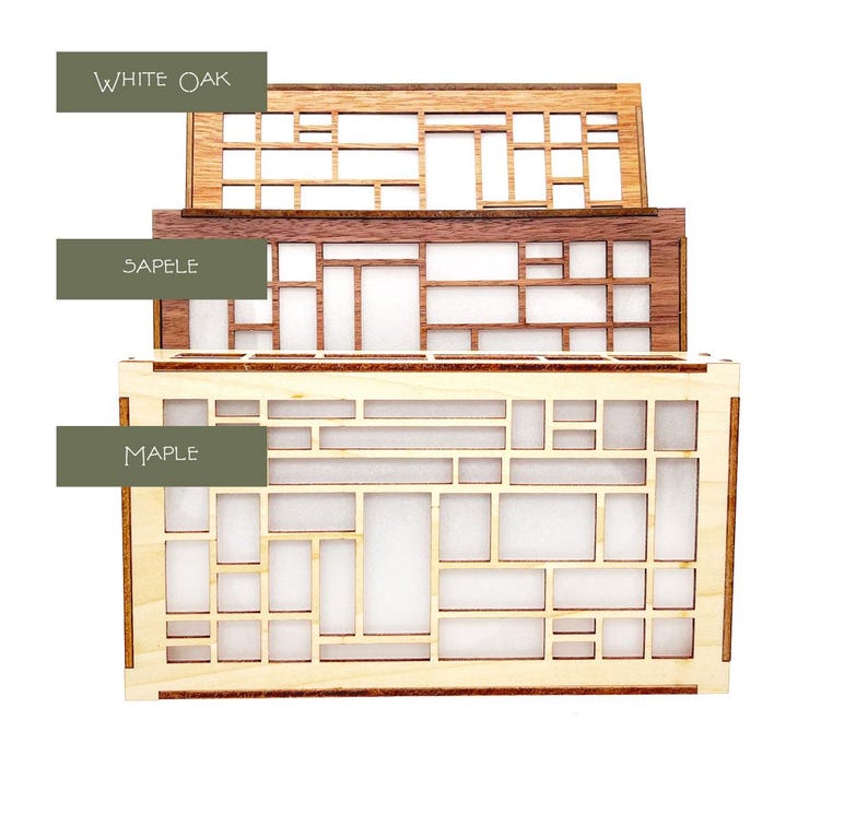 Peut inclure: Trois bo&icirc;tes en bois empil&eacute;es. La bo&icirc;te sup&eacute;rieure est en ch&ecirc;ne blanc, celle du milieu en sapelli et celle du bas en &eacute;rable. Chaque bo&icirc;te pr&eacute;sente un motif g&eacute;om&eacute;trique avec des d&eacute;coupes rectangulaires et carr&eacute;es. Le texte "WHITE OAK", "SAPELE" et "MAPLE" est visible.